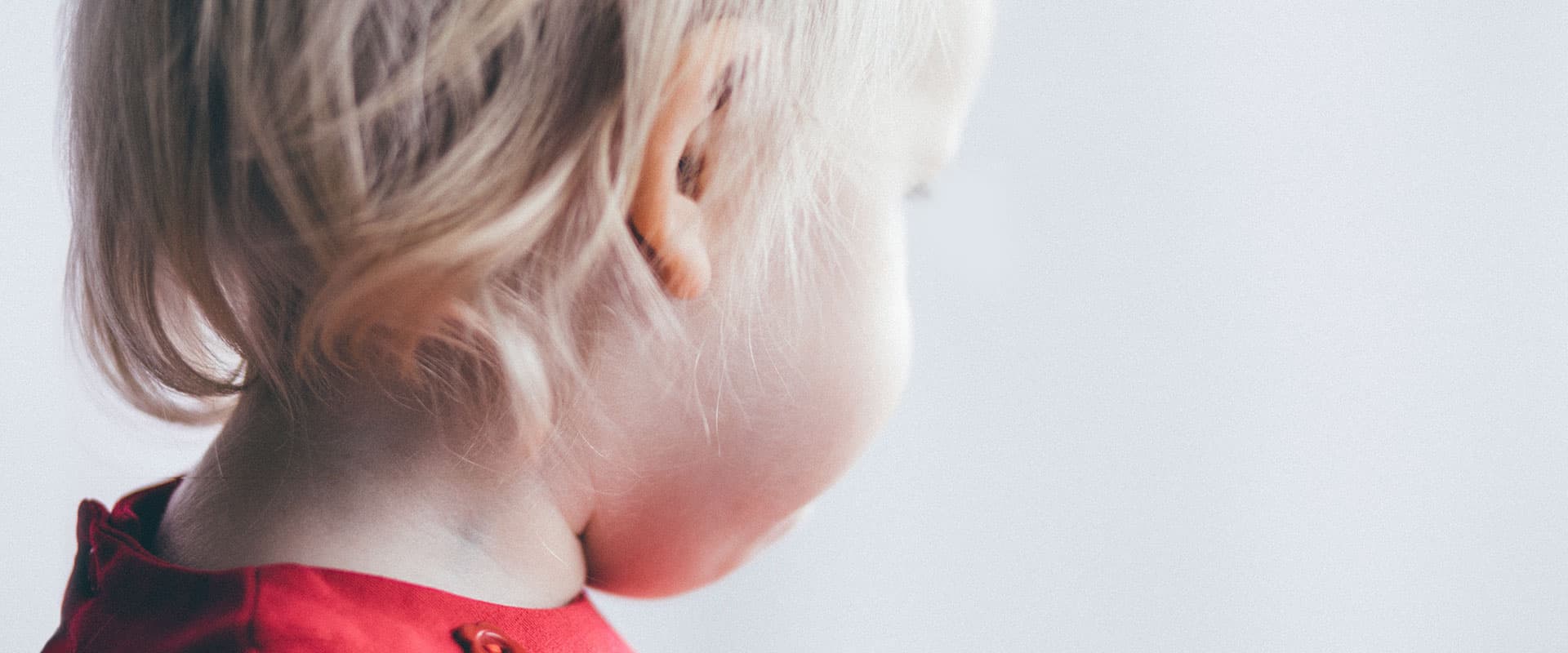 Profilen til et lite barn med lyst hår og rød genser